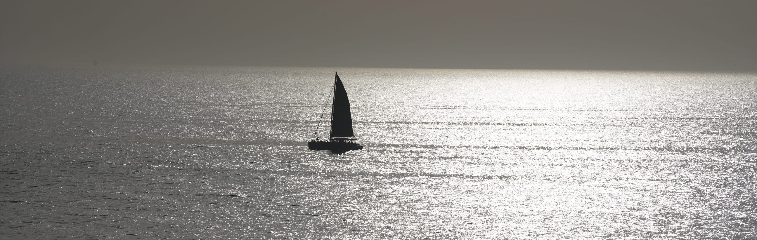 A sailboat in silhouette on a sunlit sea